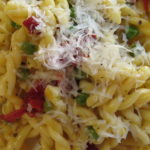 Closeup of pasta recipe with sun-dried tomatoes and peas with melting parmesan cheese.