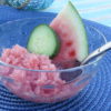 Watermelon Cucumber Granita in clear bowl with spoon and side of cucumber and watermelon slices.