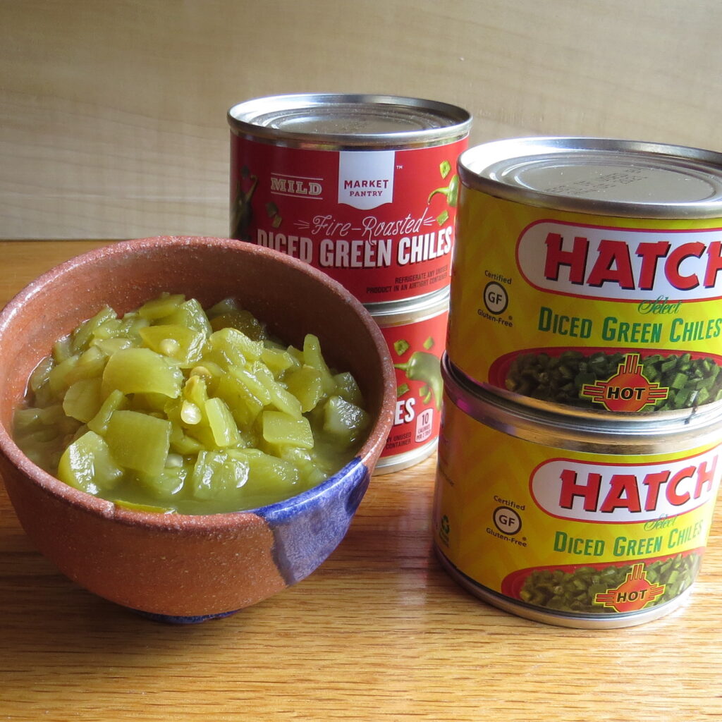 Bowl of chopped green chile with cans of two varieties of green chiles.
