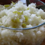 Close up of Green Chile Lime Rice in a clear bowl. Shows texture of rice with the green flecks of chiles.