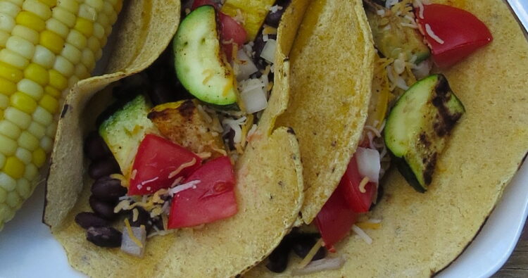 Close up photos of grilled zucchini and black bean tacos in corn tortilla with cheese and tomatoes