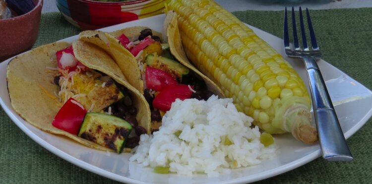Zucchini Black Bean tacos with Green Chile Lime Rice and Corn on the Cob on a white plate.