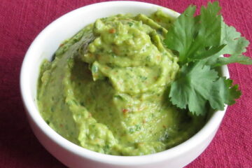 Chile Avocado Sauce in a white bowl with a sprig of cilantro sitting on a red cloth.